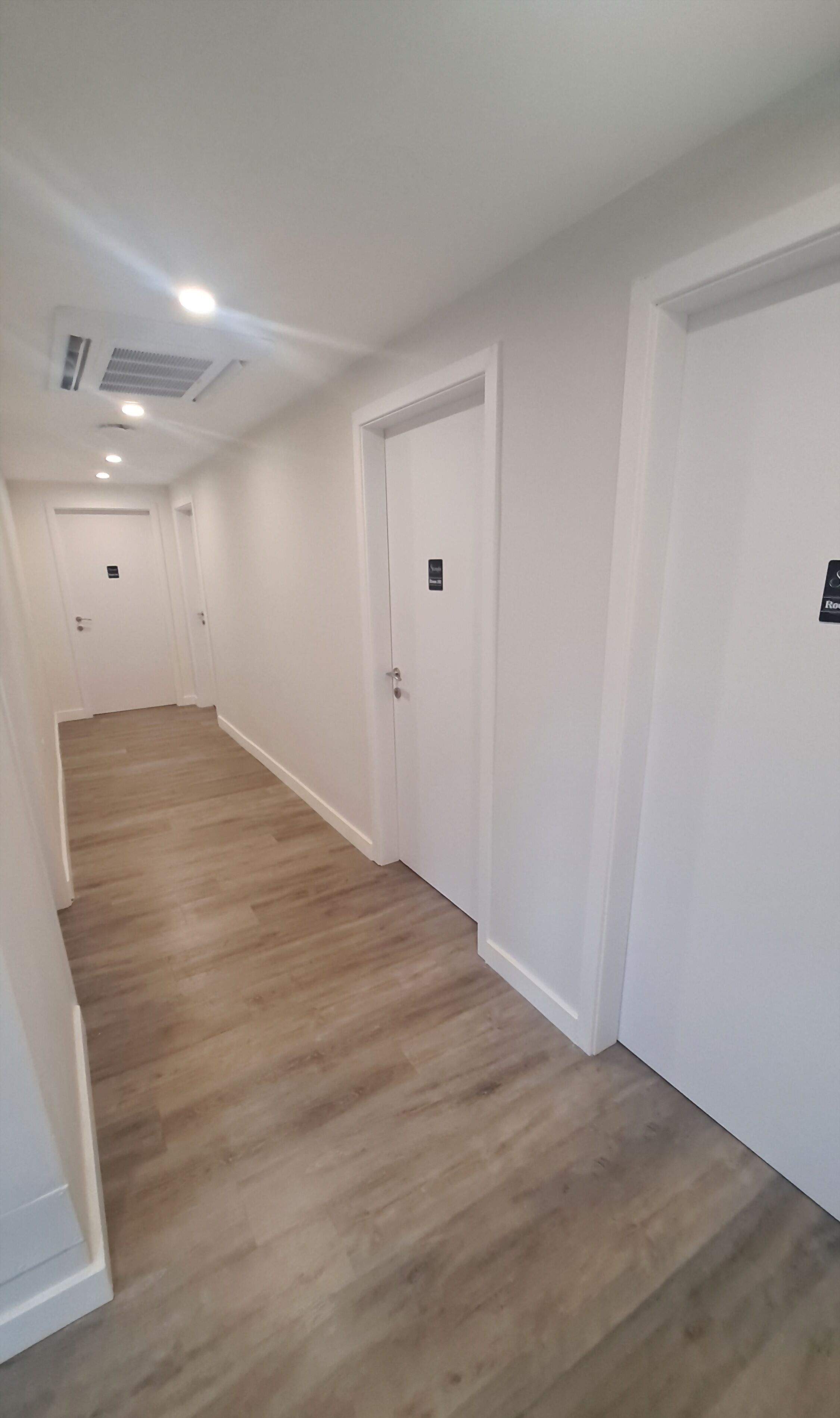 Un pasillo con suelo de madera y paredes blancas, que conduce a varias puertas.