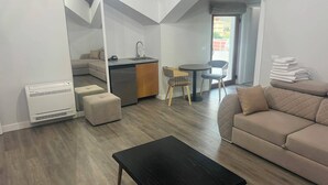 Una sala de estar moderna con una mesa de centro negra, un sofá color beige y una zona de cocina con un lavamanos y sillas.