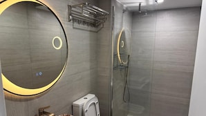 Moderni kylpyhuone, jossa on suuri peili, erillinen pesuallas, wc ja lasiseinällä varustettu suihku.