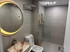 A modern bathroom with a large mirror, a vessel sink, a toilet, and a glass-enclosed shower. - Stemalu Corp  (Gjirokastër)
