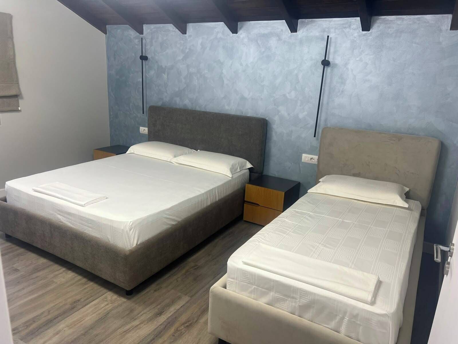 Ein Zimmer mit zwei Betten, Holzboden und einer strukturierten Wand.