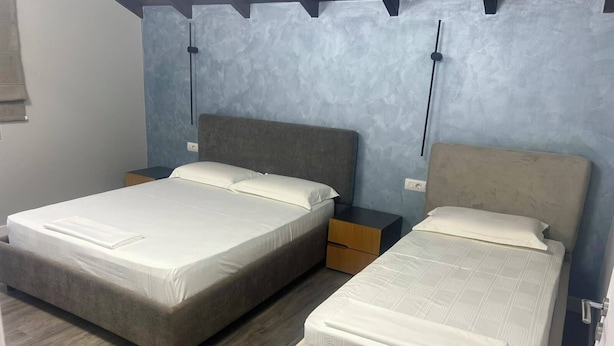 Una habitación con dos camas, piso de madera y pared con textura.