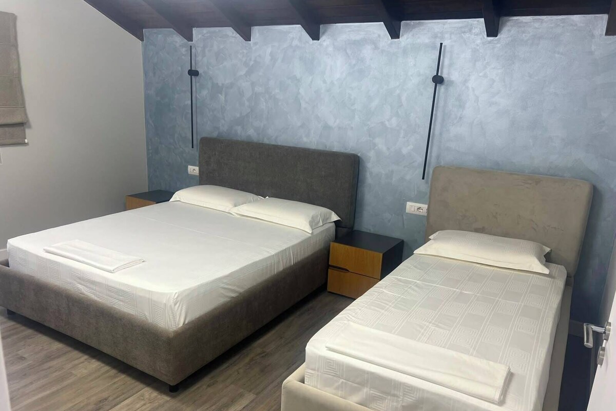 A room with two beds, wooden flooring, and a textured wall.