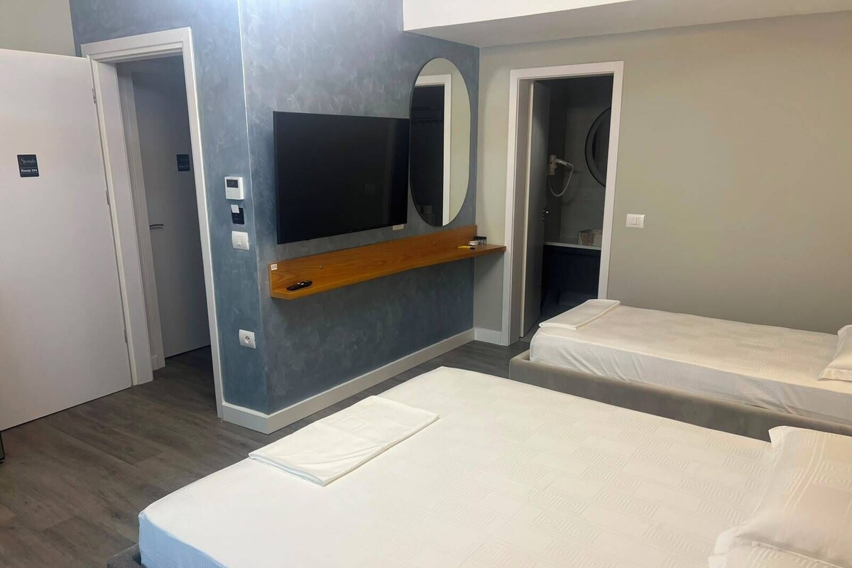 A hotel room with two beds, a TV mounted on the wall, a mirror, and a wooden shelf.