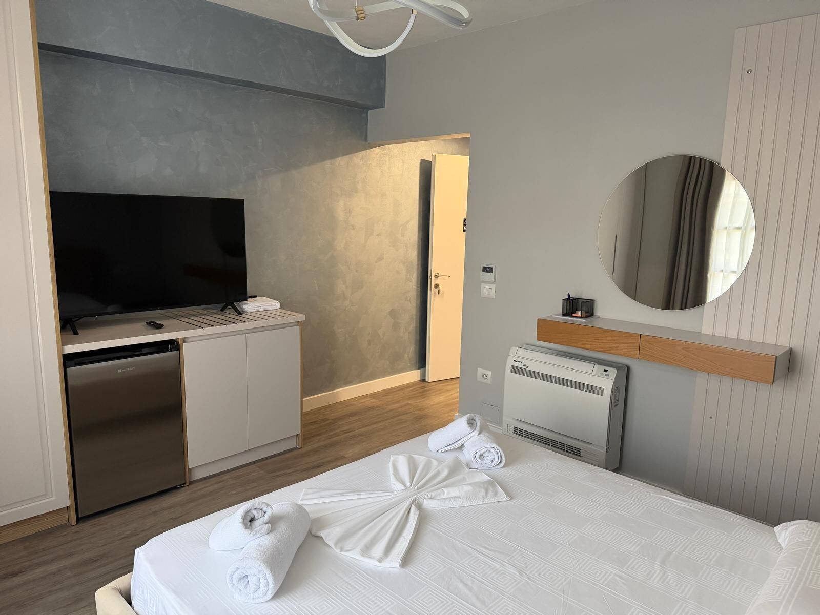 A hotel room with a bed, a television, a minibar, a mirror, and a bathroom.