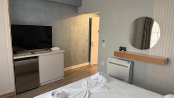A hotel room with a bed, a television, a minibar, a mirror, and a bathroom.
