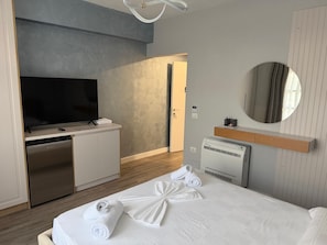 Habitación de hotel con cama, televisión, minibar, espejo y baño.