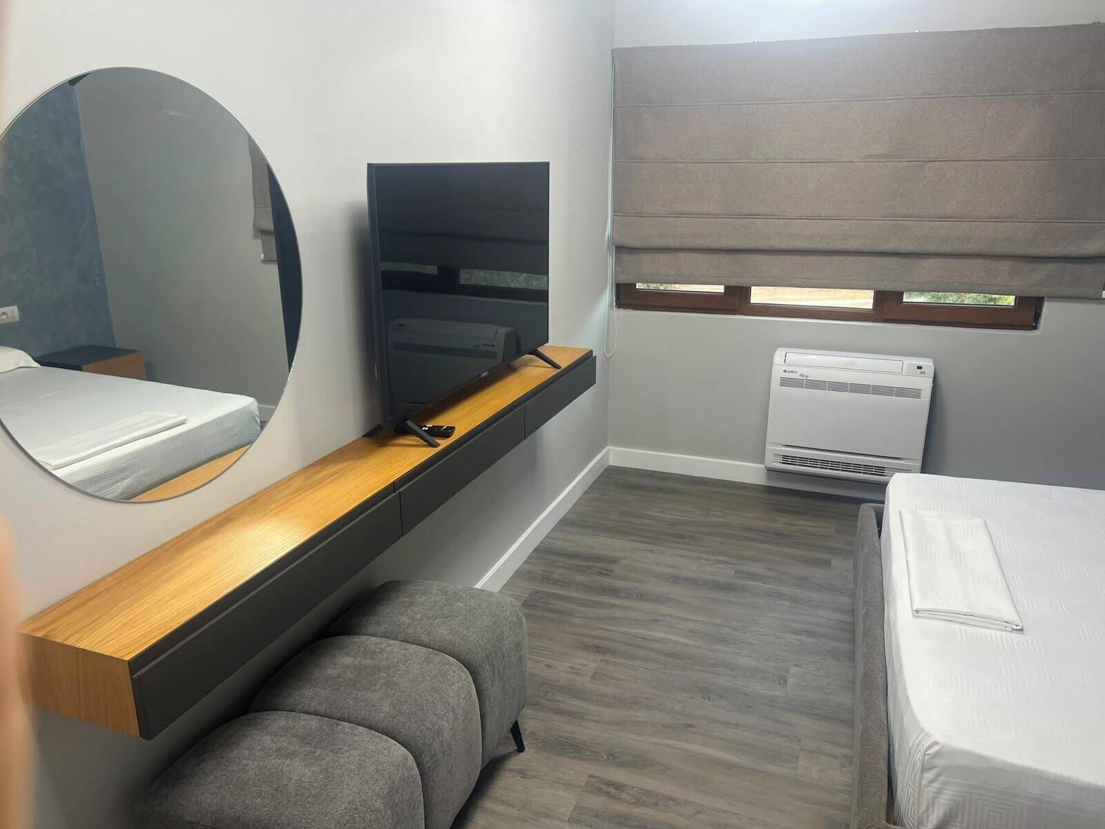 Une chambre de taille modeste comprenant un lit, un petit coin salon, un téléviseur et une fenêtre avec un store.
