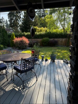 Een houten terras met een tafel en stoelen, omgeven door groen en een houten omheining.