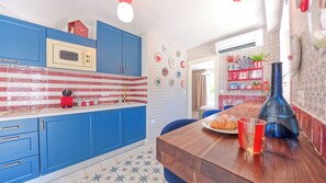 Eine Küche mit blauen Schränken, einem roten Wasserkocher und einem Holztisch mit einem Croissant und einer roten Tasse.