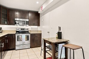 A compact kitchen with dark wood cabinets, stainless steel appliances, a granite countertop, and a small dining area with stools. - Spacious & Modern apt for a family beach vacation (Hollywood)
