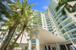 Ein modernes Hotel mit einer geschwungenen Fassade, mehreren Balkonen und Palmen.