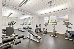 A gym with various exercise equipment, large windows, and a flat-screen TV. - Spacious & Modern apt for a family beach vacation (Hollywood)