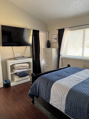 A bedroom with a bed, a television mounted on the wall, a dresser, and a window with curtains. - Sunny Getaway at Sports Village (St. George)