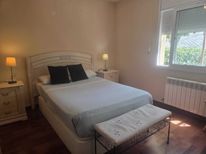 Ein Schlafzimmer mit einem Bett, Nachttischen, einer Bank, einem Fenster und einer Heizung.