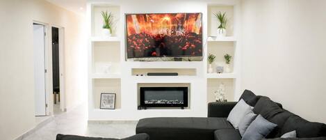 Un salon moderne doté d’un grand téléviseur à écran plat fixé au mur, d’un canapé en cuir noir et d’une cheminée située sous le téléviseur.