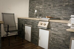 Een kitchenette met een gasfornuis, een spoelbak en een metalen stoel.