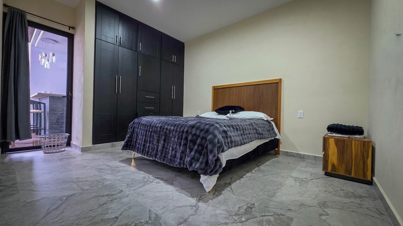 A bedroom with a bed, dark wardrobe, and a small wooden side table.