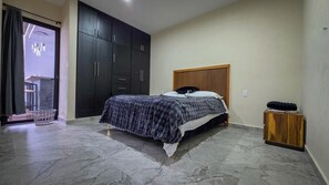 Een slaapkamer met een bed, een donkere garderobe en een klein houten nachtkastje.