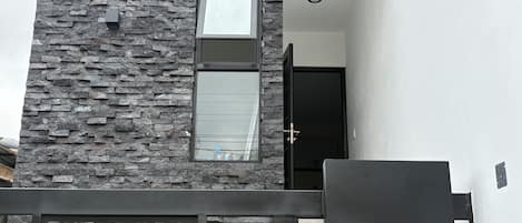 Un edificio moderno con fachada de piedra, una puerta negra y un portón metálico geométrico.