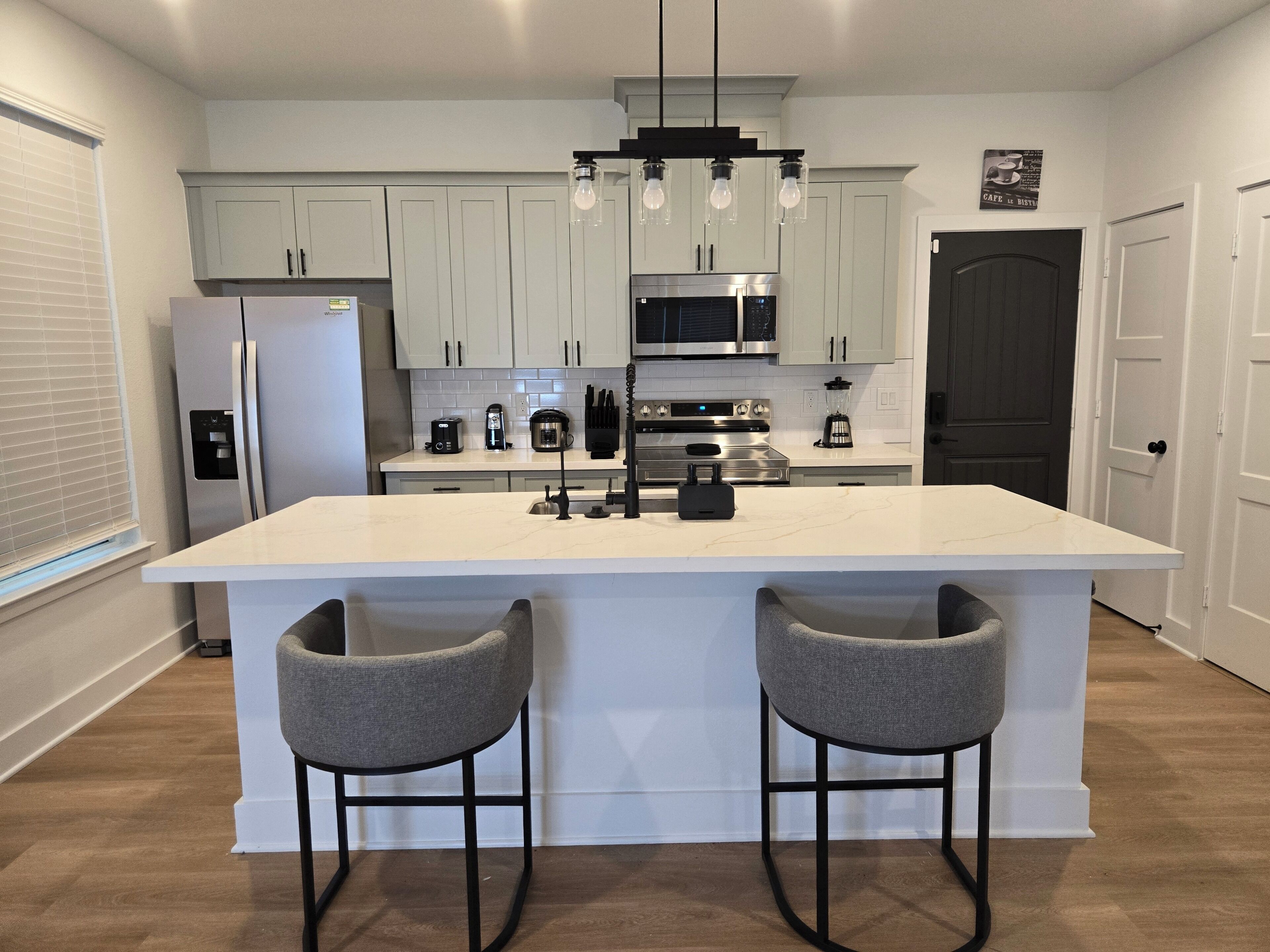 Een moderne keuken met een centraal eiland, barkrukken, roestvrijstalen apparatuur en een hanglamp.