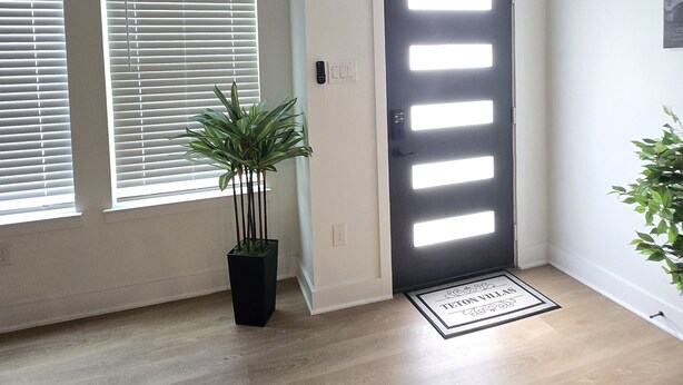 Un interior moderno con suelo de madera, una puerta de marco negro y una planta en maceta.