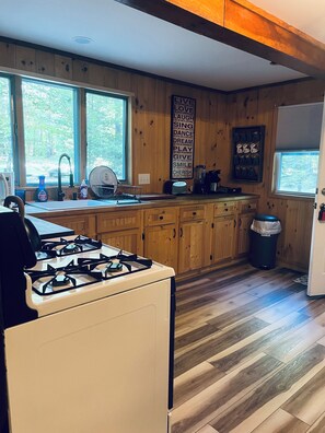 Una cocina con armarios de madera, una estufa a gas, un fregadero y una ventana con vistas a árboles.