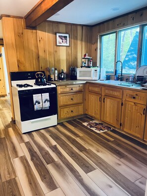 A kitchen with wooden cabinets, a stove, a microwave, and a window with a view of trees.