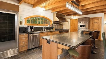 Une cuisine avec des poutres en bois, un îlot central en pierre, des appareils électroménagers en acier inoxydable et une grande fenêtre.