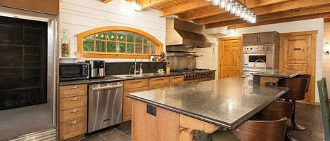 A kitchen with wooden beams, a stone island, stainless steel appliances, and a large window.
