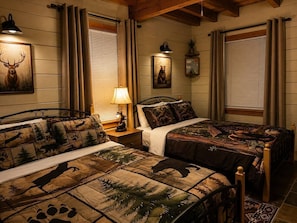 A room with two beds, a nightstand, a lamp, and a wall with framed pictures.