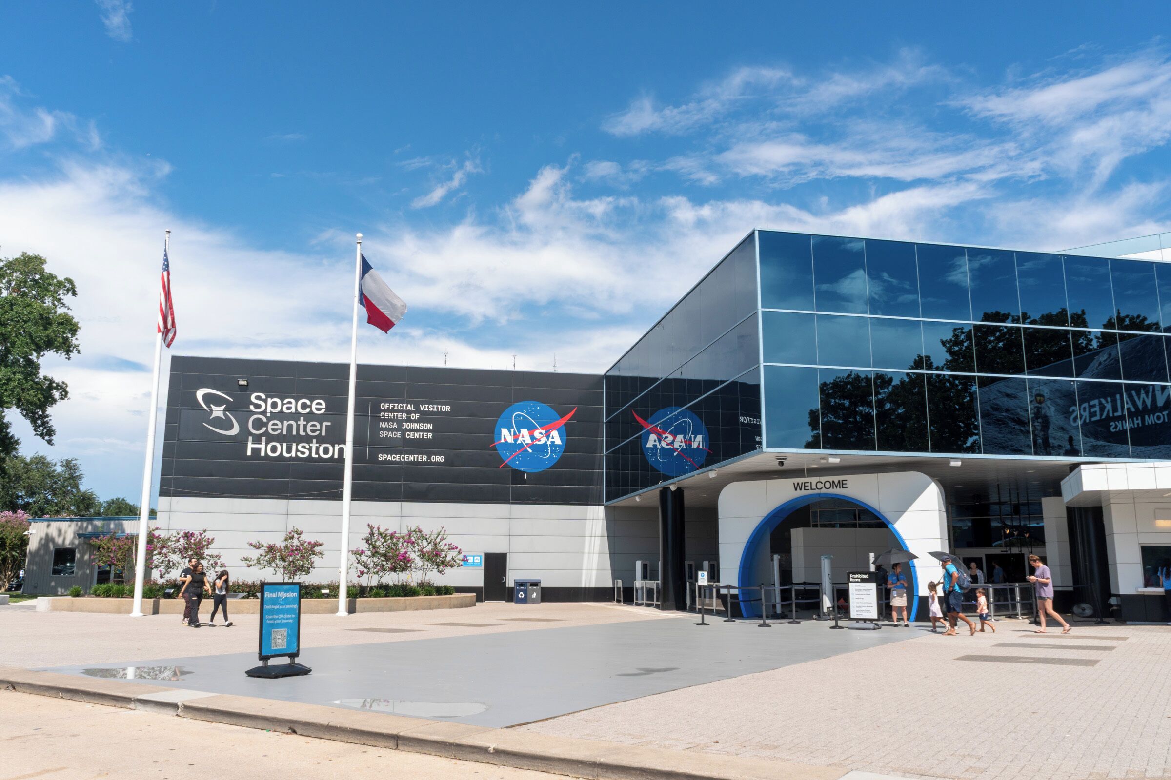 The Space Center Houston building with NASA and ARMS logos, a flag, and a sign for the final mission.