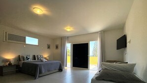 Een slaapkamer met een bed, nachtkastje, televisie en een schuifpui naar een balkon.