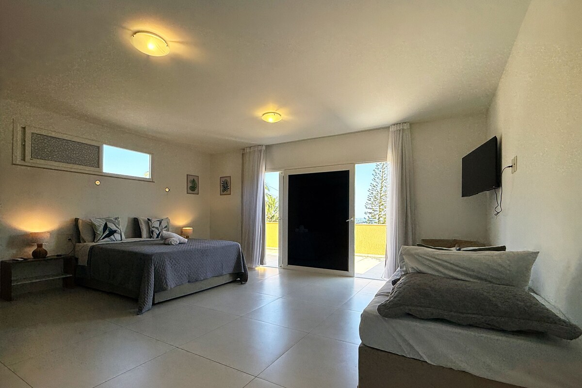 Un dormitorio con cama, mesita de noche, televisor y puerta corrediza a un balcón.