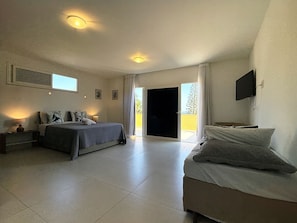 Un dormitorio con cama, mesita de noche, televisor y puerta corrediza a un balcón.