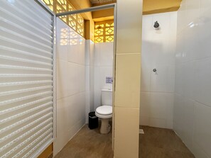 Un baño pequeño y cerrado con inodoro, un bote de basura y zona de ducha.