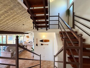 A multi-level interior with a wooden staircase, a ceiling with a woven pattern, and a wall with mounted paddles. - Villa em João Fernandes com Piscina (Buzios)