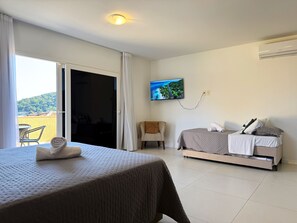 A hotel room with a bed, a TV, a chair, and a balcony with a view. - Villa em João Fernandes com Piscina (Buzios)