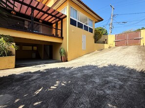 Edifici de dues plantes amb un balcó cobert, una escala que mena a un garatge i un vial pavimentat.