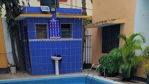 En swimmingpool med ett kaklat poolområde, en liten byggnad med en skylt och krukväxter.