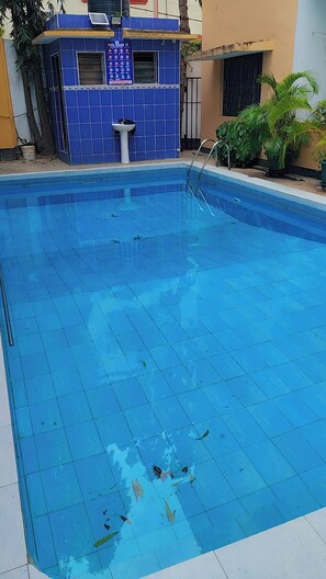 A swimming pool with a tiled deck, a small building with a sign, and potted plants. - Comfortable and safe place not to far from the beach and it is family friendly. (Mombasa)