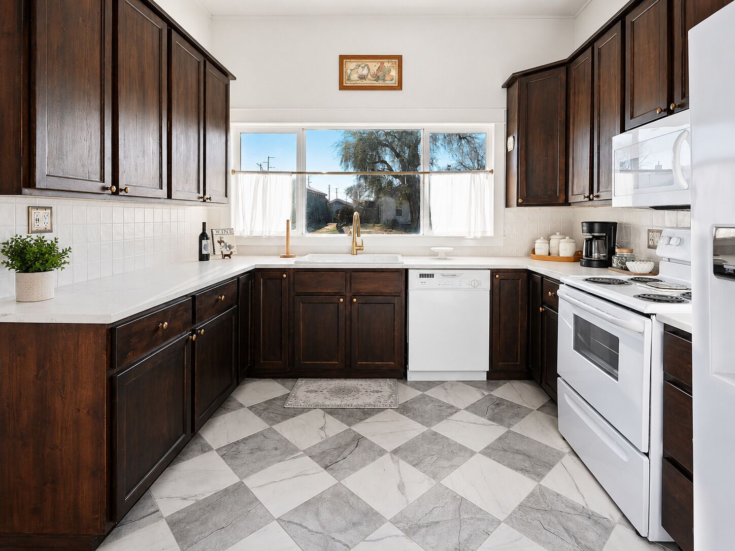 A kitchen with dark wooden cabinets, a white countertop, a dishwasher, a stove, and a window with a view of trees.