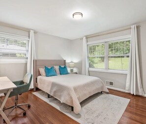 Habitación de hotel con cama, escritorio, silla y ventana con cortinas.