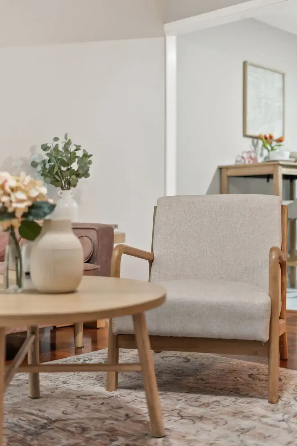 Una habitación con una mesa redonda de madera, un sillón color beige y un tapete estampado.