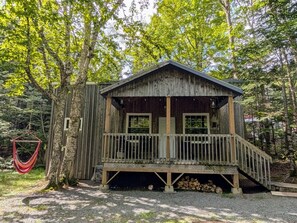 Une cabane en bois avec un porche, entourée d’arbres.