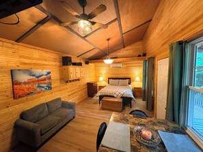 L’intérieur d’un chalet en bois, avec un lit, un canapé, une table à manger et un tableau accroché au mur.