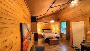 A cozy wooden cabin bedroom with a bed, bedside lamps, a bench, and a painting on the wall.