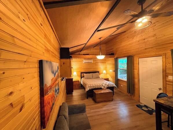 A cozy wooden cabin bedroom with a bed, bedside lamps, a bench, and a painting on the wall.
