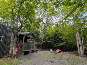 A cabin with a porch and a deck, surrounded by a forest.