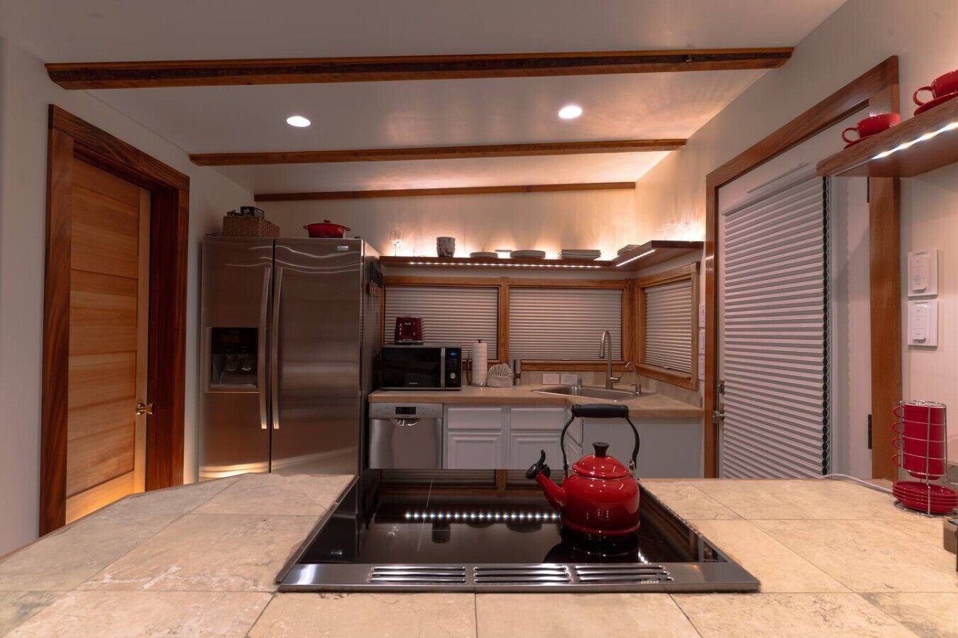 Una cocina moderna con estufa integrada, electrodomésticos de acero inoxidable y un hervidor rojo.